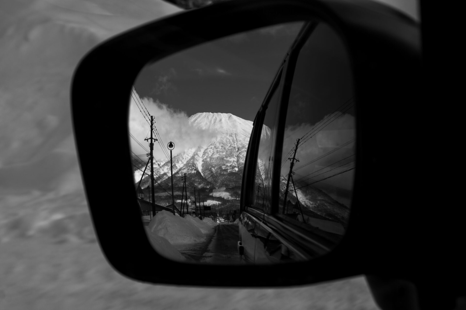Un vulcano innevato riflesso nello specchietto del van, sulla strada verso il resort